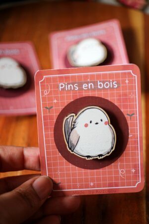 Photo d'un pin's en bois d'érable représentant un shima enaga, posé sur un tissu, montrant le grain naturel du bois.