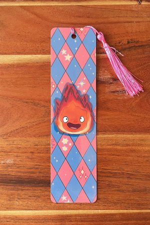 marque-page illustré avec le personnage Calcifer sur un fond à losanges bleus et roses, avec un pompon rose