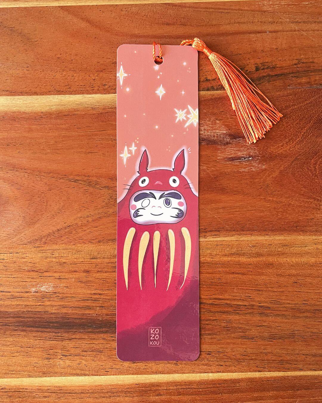 marque-page illustré représentant un totoro deguisé en daruma, avec un pompon orange