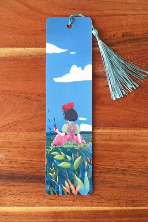 marque-page illustré représentant Kiki la petite sorcière de dos dans un champ de fleurs, avec un pompon bleu clair,