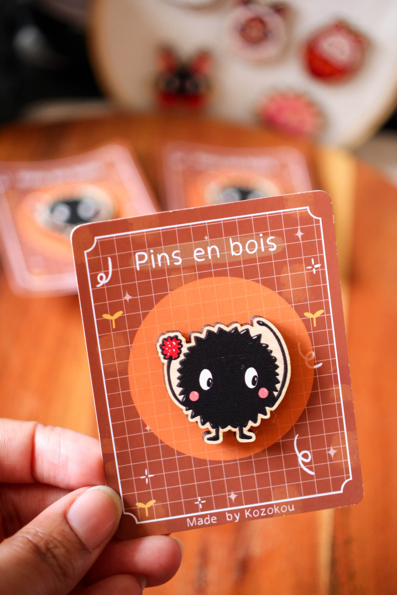 Photo d'un pin's en bois d'érable représentant une noiraude, posé sur un tissu, montrant le grain naturel du bois.
